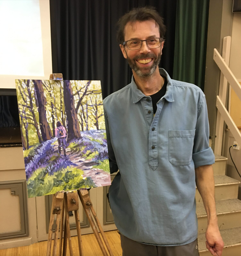An artist stands by his painting on an easel.